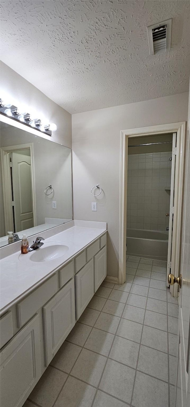 bathroom featuring tile patterned floors, vanity, a textured ceiling, and tiled shower / bath