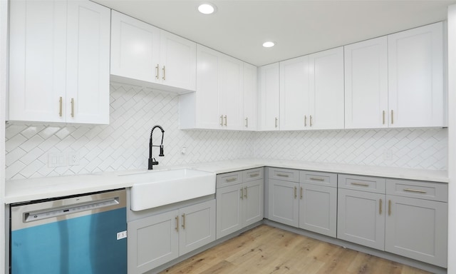 kitchen featuring gray cabinetry, sink, stainless steel dishwasher, decorative backsplash, and light wood-type flooring