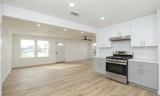 kitchen with light wood-type flooring, backsplash, gas range, ceiling fan, and white cabinets