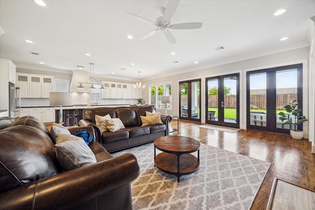 living room with french doors, ornamental molding, ceiling fan with notable chandelier, sink, and hardwood / wood-style floors