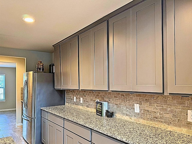 kitchen with tasteful backsplash, baseboards, freestanding refrigerator, light stone countertops, and recessed lighting