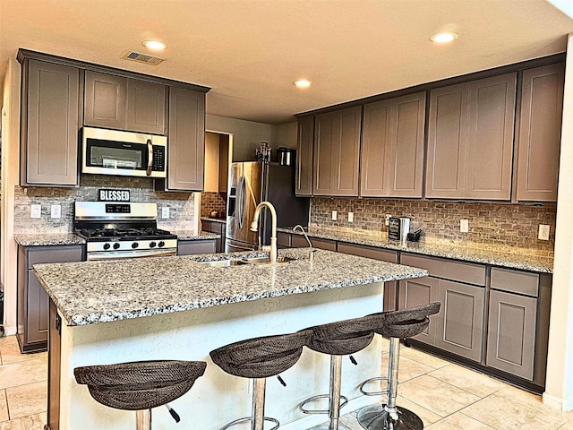 kitchen with stainless steel appliances, light stone counters, an island with sink, and a sink