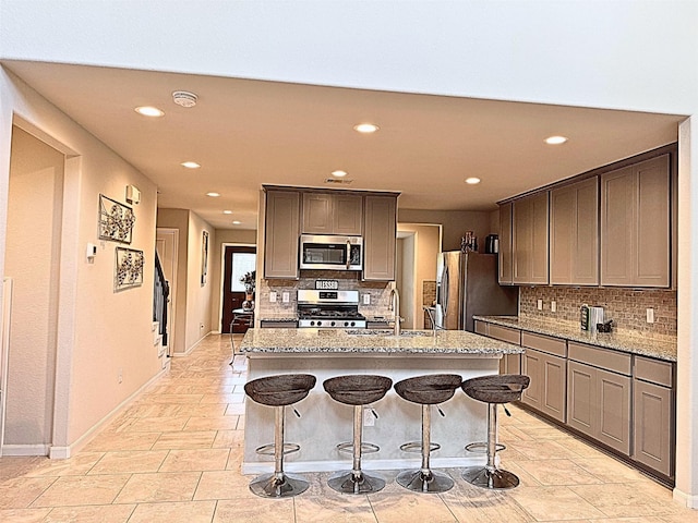 kitchen featuring an island with sink, appliances with stainless steel finishes, a breakfast bar, light stone counters, and a sink