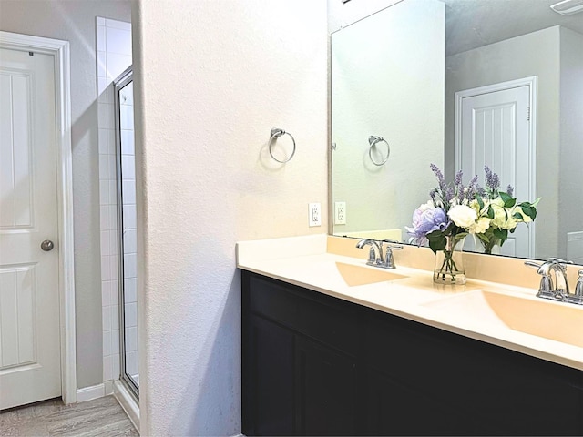 bathroom featuring double vanity, wood finished floors, a sink, and a shower stall