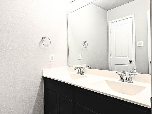 full bath with a textured wall, double vanity, and a sink