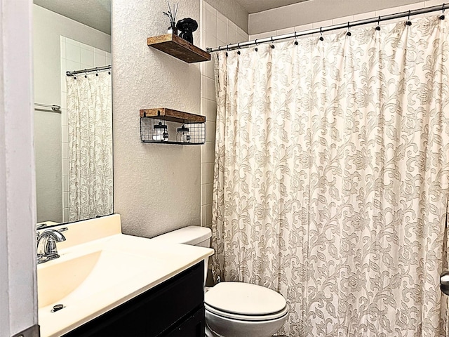 bathroom with a textured wall, vanity, toilet, and a textured ceiling