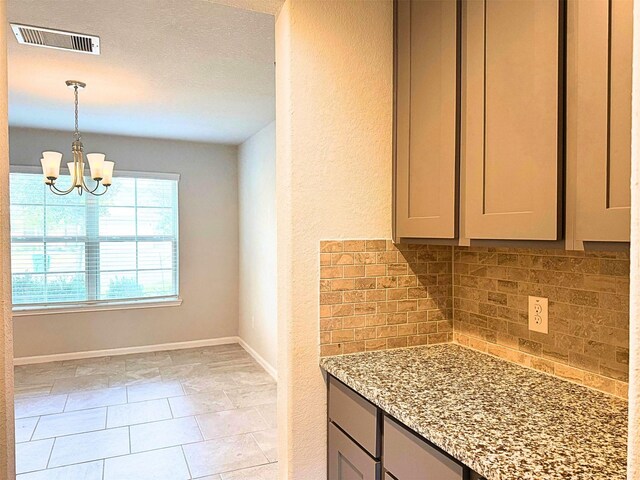 kitchen with visible vents, light stone counters, backsplash, gray cabinets, and a notable chandelier