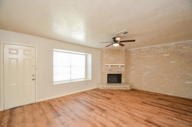 unfurnished living room featuring a brick fireplace, light hardwood / wood-style flooring, ceiling fan, a textured ceiling, and brick wall