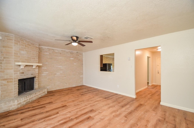 unfurnished living room featuring ceiling fan, a fireplace, light wood-type flooring, and a textured ceiling