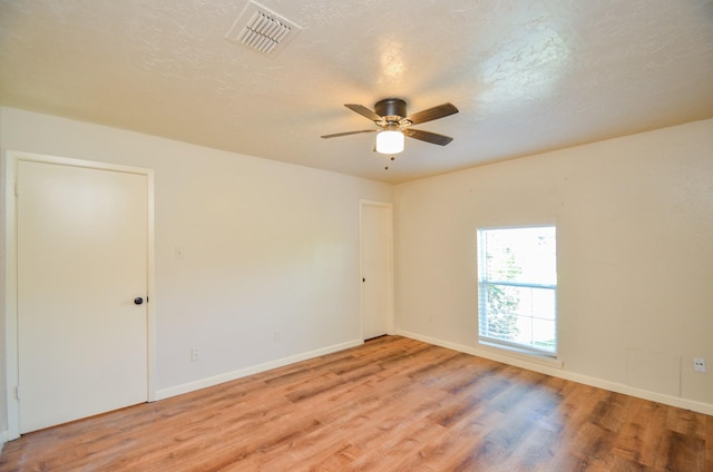 empty room with a textured ceiling, light wood-type flooring, and ceiling fan