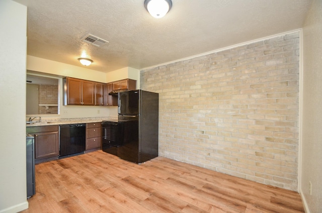 kitchen with brick wall, light wood-type flooring, and black appliances