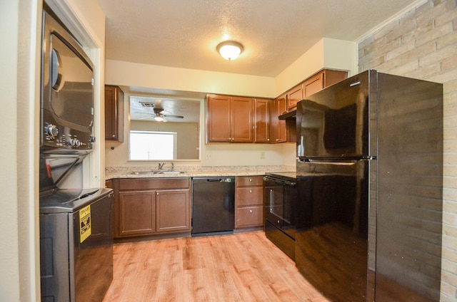 kitchen featuring light wood-type flooring, ceiling fan, sink, black appliances, and stacked washer and clothes dryer