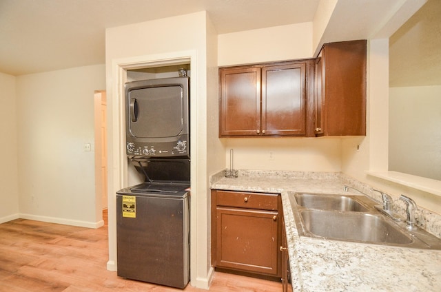 kitchen with light wood-type flooring, stacked washing maching and dryer, and sink