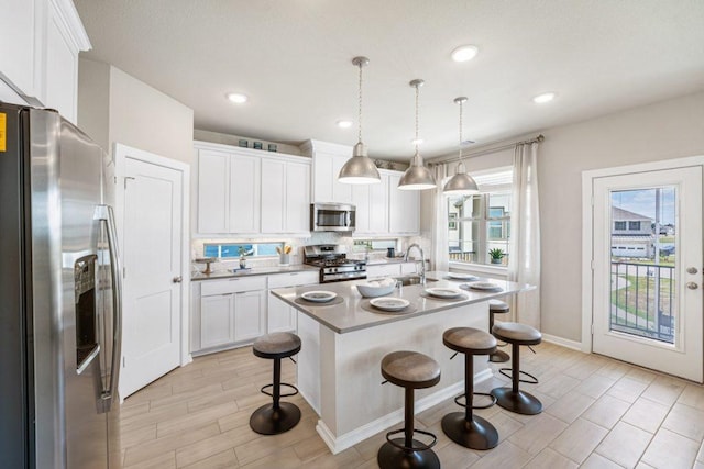 kitchen featuring a kitchen breakfast bar, pendant lighting, a kitchen island with sink, white cabinets, and appliances with stainless steel finishes