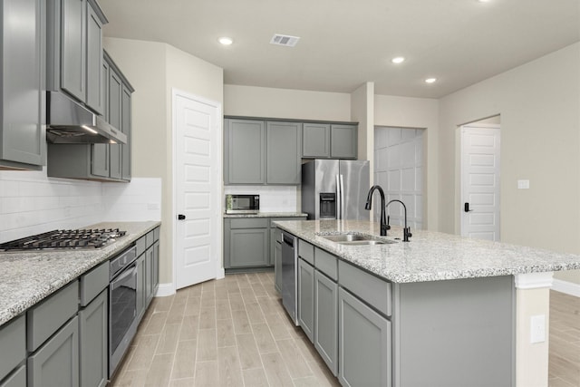 kitchen featuring gray cabinetry, sink, backsplash, an island with sink, and appliances with stainless steel finishes