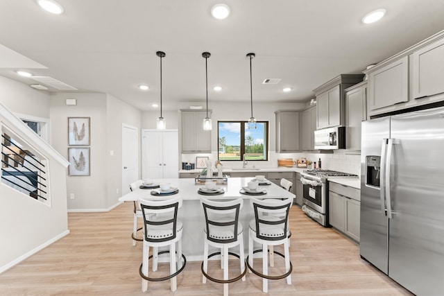 kitchen with a center island, hanging light fixtures, gray cabinets, light wood-type flooring, and appliances with stainless steel finishes