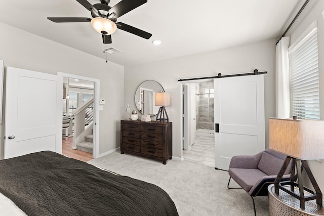 bedroom featuring light carpet, a barn door, ensuite bathroom, and ceiling fan