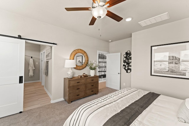 bedroom with a barn door, ceiling fan, and light carpet