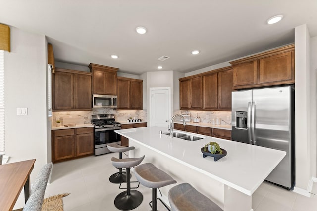 kitchen featuring sink, an island with sink, appliances with stainless steel finishes, tasteful backsplash, and a breakfast bar area