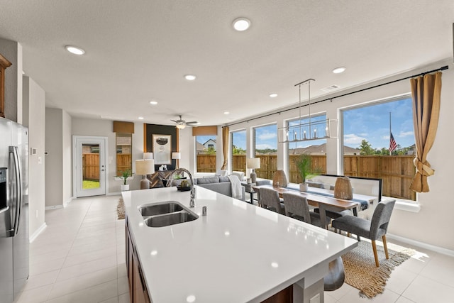 kitchen with stainless steel fridge, sink, hanging light fixtures, plenty of natural light, and an island with sink