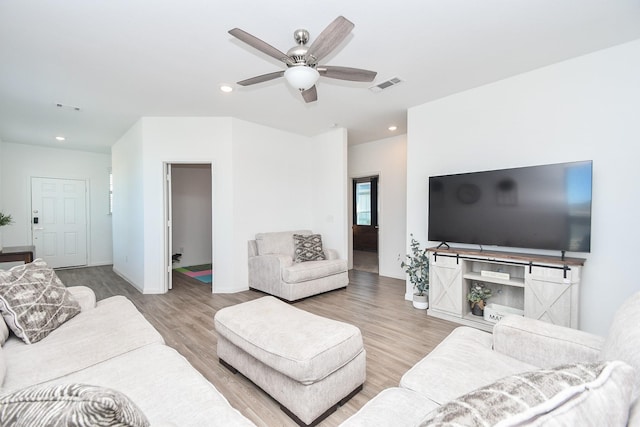 living room with ceiling fan, a barn door, and light hardwood / wood-style flooring