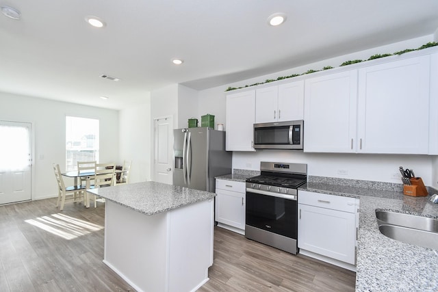 kitchen featuring stainless steel appliances, white cabinetry, a kitchen island, and sink