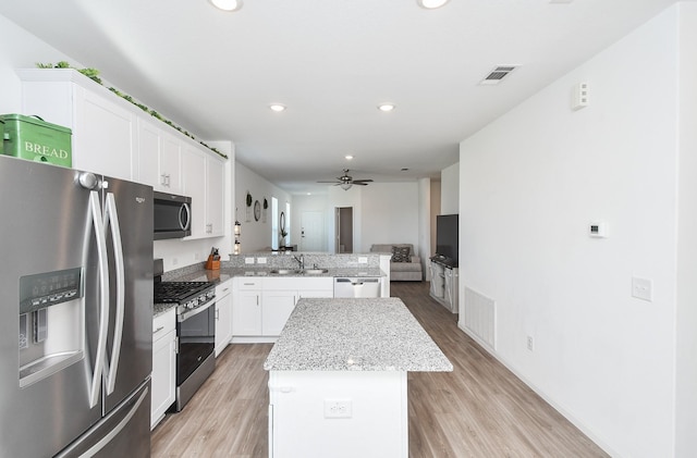 kitchen featuring light stone countertops, appliances with stainless steel finishes, ceiling fan, a center island, and white cabinetry