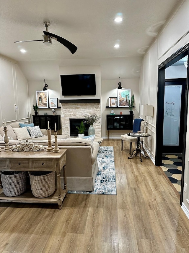 living room with ceiling fan, a fireplace, and light hardwood / wood-style floors