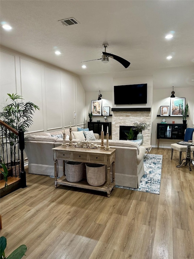 living room featuring light hardwood / wood-style flooring, a stone fireplace, and ceiling fan