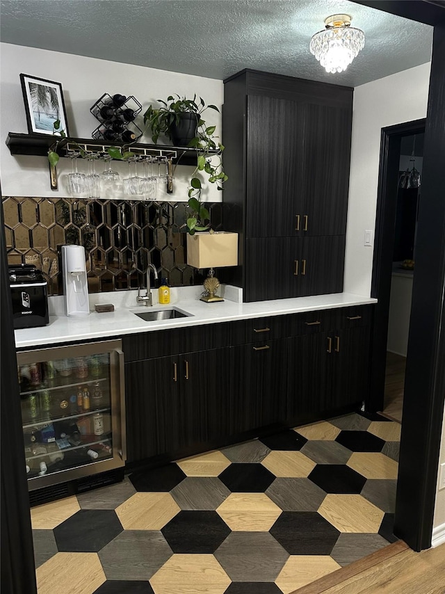 bar featuring a textured ceiling, tasteful backsplash, beverage cooler, and sink