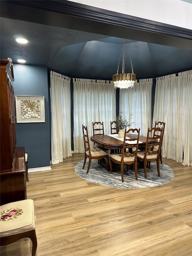 dining area with light hardwood / wood-style floors, vaulted ceiling, and a notable chandelier