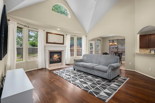 living room with a notable chandelier, a healthy amount of sunlight, dark wood-type flooring, and a tiled fireplace