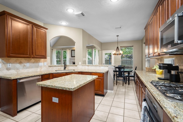 kitchen with sink, a notable chandelier, backsplash, a kitchen island, and appliances with stainless steel finishes