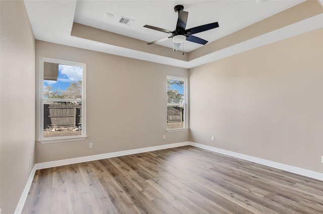 empty room featuring ceiling fan, light wood-type flooring, and a tray ceiling