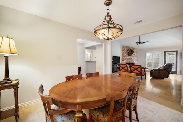 dining room with ceiling fan, vaulted ceiling, and a brick fireplace