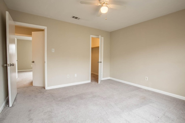 unfurnished bedroom with a walk in closet, ceiling fan, light colored carpet, and a closet