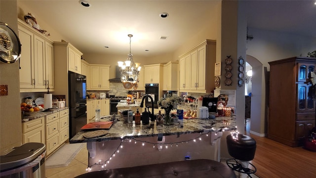 kitchen featuring a breakfast bar, cream cabinets, black appliances, decorative light fixtures, and kitchen peninsula