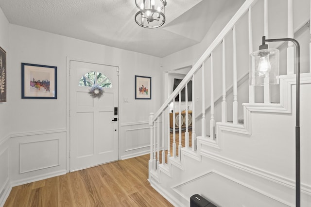 foyer with a notable chandelier, light wood-type flooring, and a textured ceiling