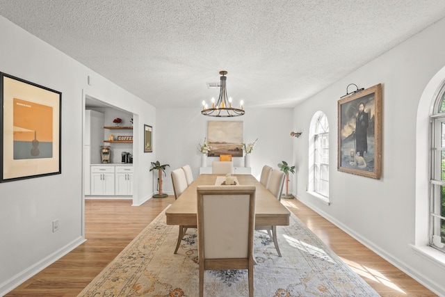 dining space with a chandelier, a textured ceiling, and light wood-type flooring