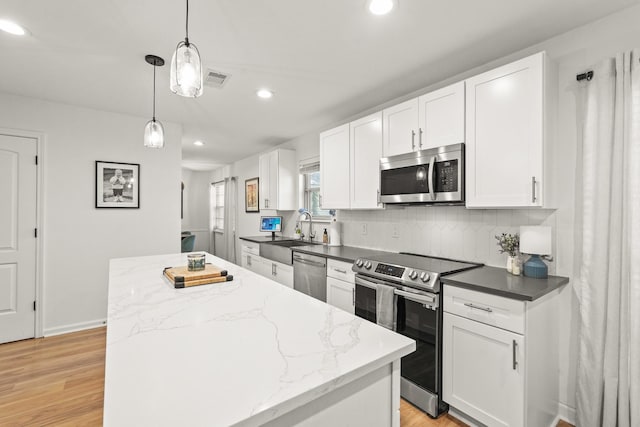 kitchen featuring appliances with stainless steel finishes, backsplash, decorative light fixtures, white cabinets, and a kitchen island