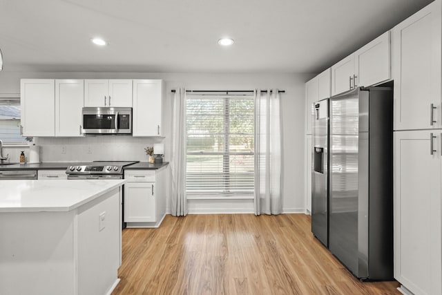 kitchen with backsplash, dark stone counters, stainless steel appliances, light hardwood / wood-style flooring, and white cabinetry