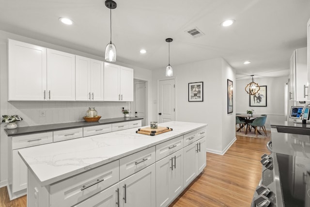 kitchen with white cabinets, light wood-type flooring, a center island, and decorative light fixtures