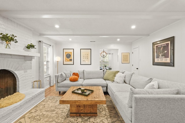 living room featuring ornamental molding, beamed ceiling, light wood-type flooring, and a brick fireplace