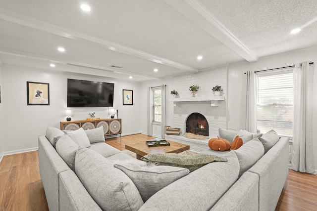 living room featuring beamed ceiling, light hardwood / wood-style floors, and a brick fireplace