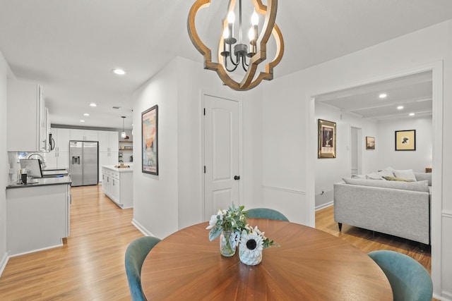 dining area with sink, a chandelier, and light wood-type flooring