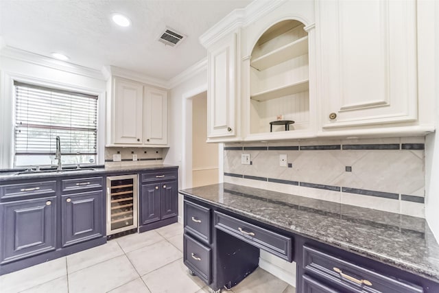 kitchen featuring sink, ornamental molding, beverage cooler, white cabinets, and dark stone counters