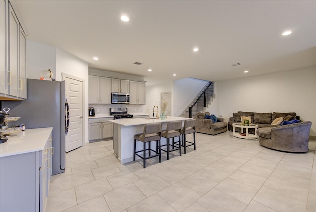 kitchen featuring sink, stainless steel appliances, gray cabinets, a breakfast bar, and a center island with sink