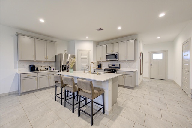 kitchen featuring sink, stainless steel appliances, a breakfast bar area, gray cabinets, and a center island with sink