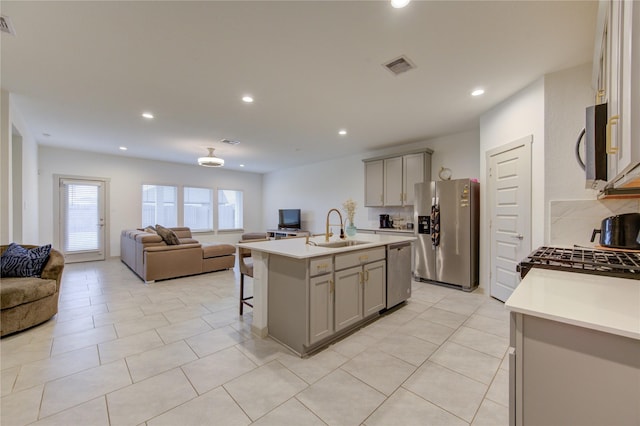 kitchen featuring a kitchen island with sink, sink, a breakfast bar area, gray cabinets, and stainless steel appliances