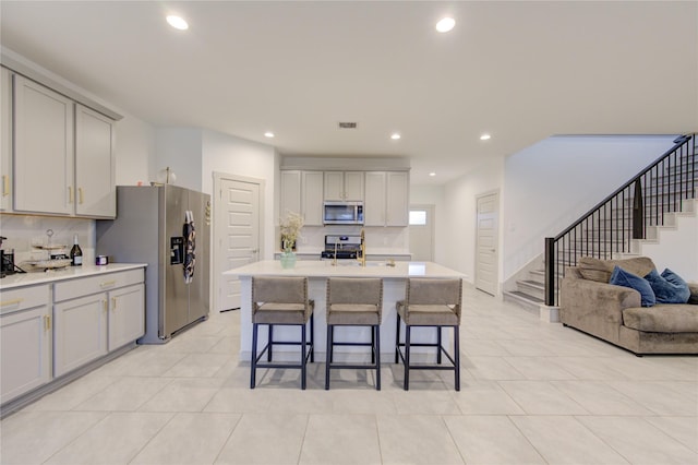 kitchen featuring a kitchen breakfast bar, tasteful backsplash, gray cabinets, a center island with sink, and appliances with stainless steel finishes